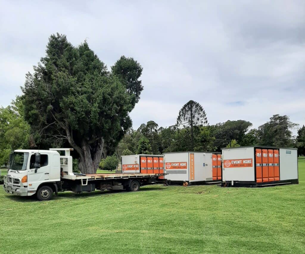 A truck on green grass picking up hired portable toilets
